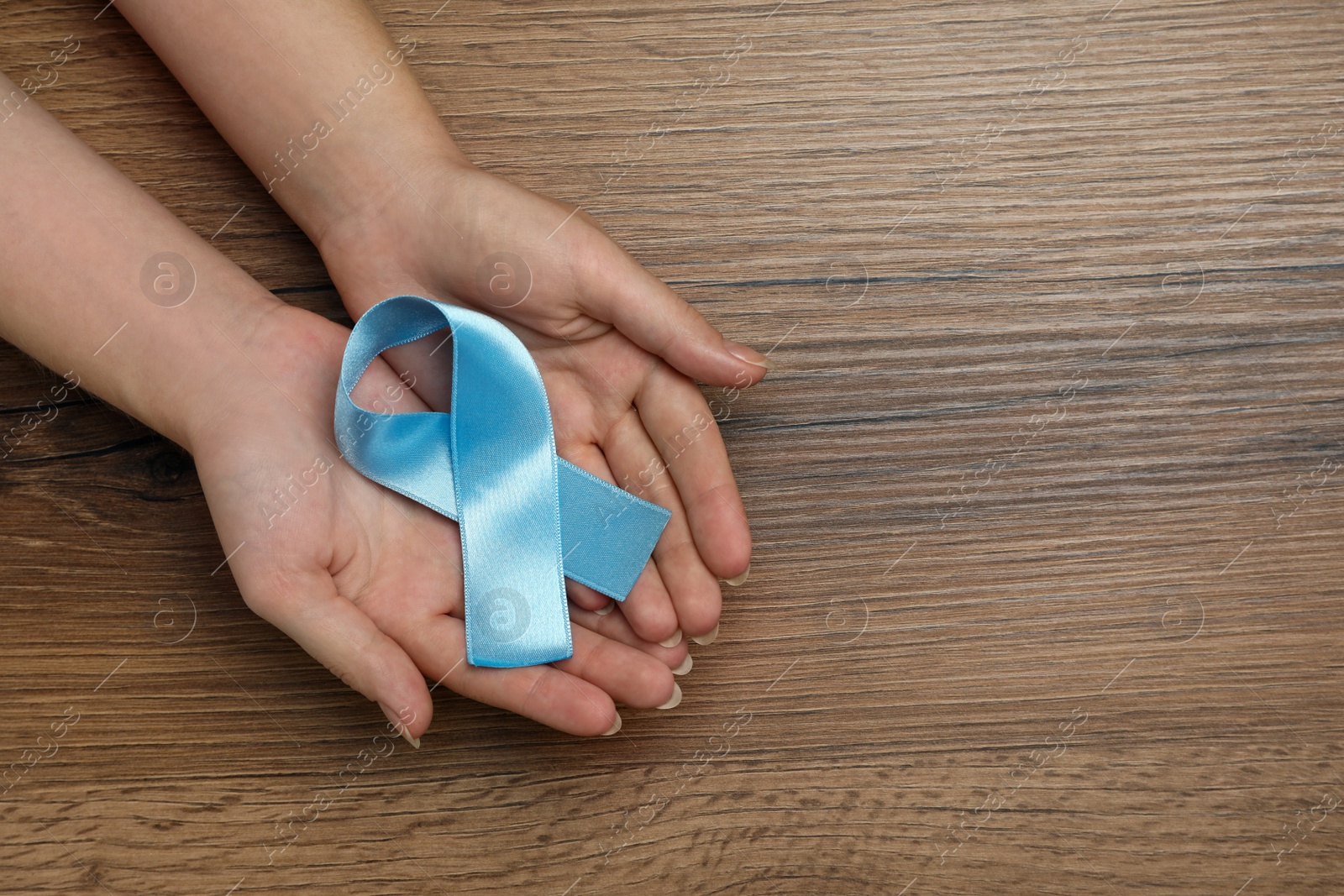 Photo of Woman holding light blue awareness ribbon at wooden table, top view. Space for text