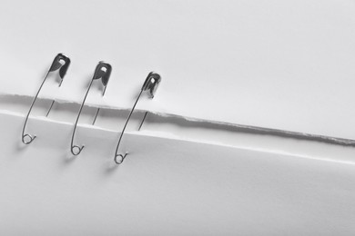 Photo of Pieces of paper sheets joined with safety pins on white background, closeup