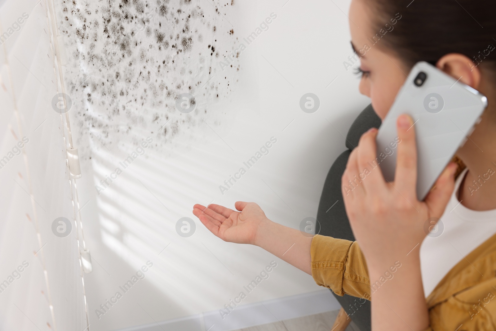 Image of Mold removal service. Woman talking on phone and looking at affected wall in room