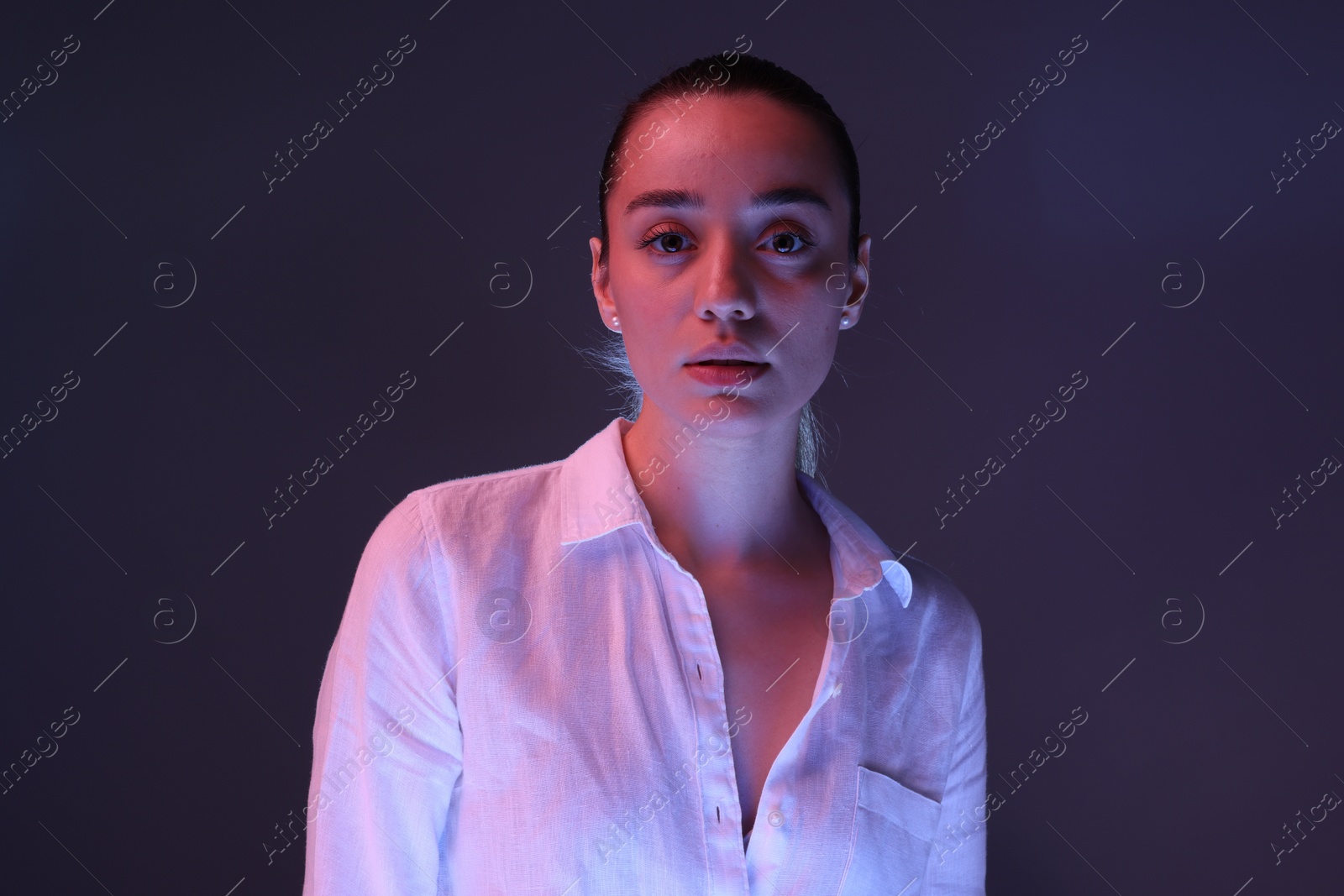 Photo of Portrait of beautiful young woman on dark purple background with neon lights