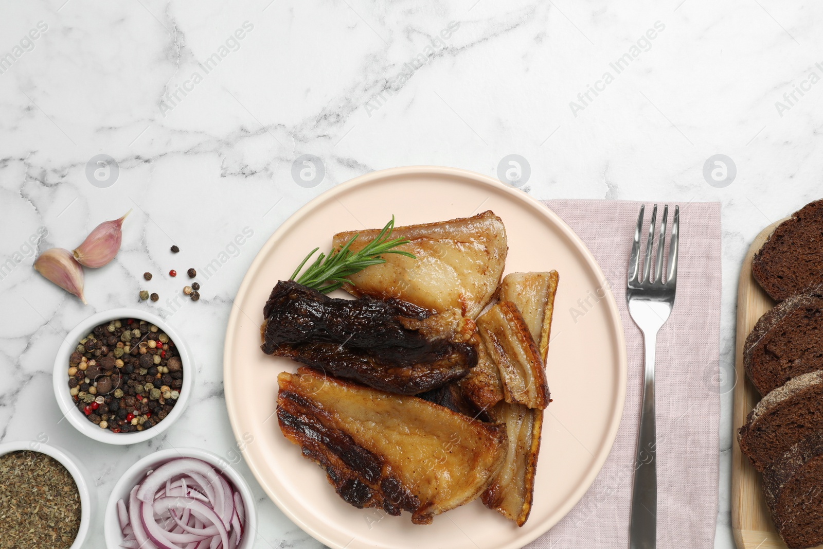 Photo of Tasty fried pork lard with rosemary on white marble table, flat lay