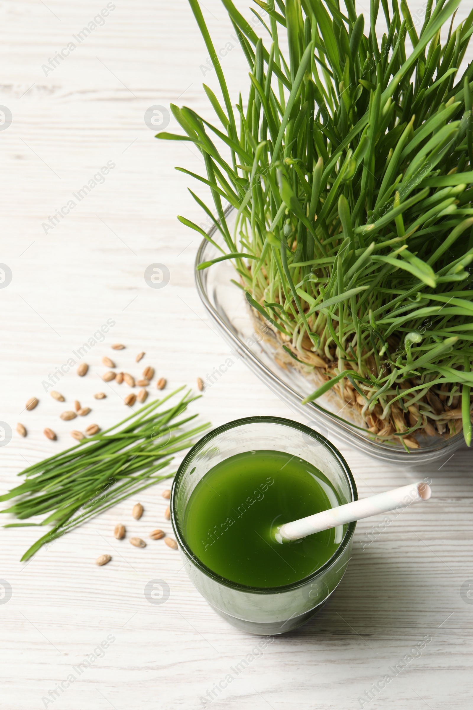 Photo of Wheat grass drink in glass, seeds and fresh green sprouts on white wooden table, flat lay