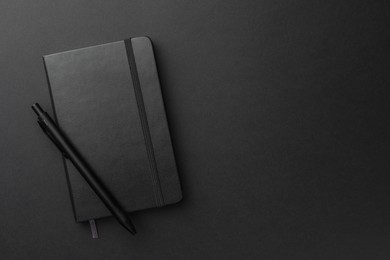 Photo of Closed notebook and pen on black background, top view. Space for text
