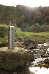 Photo of Metallic thermos on stone near river, space for text