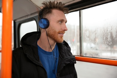 Young man listening to music with headphones in public transport. Space for text