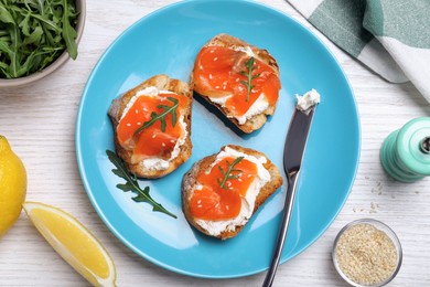 Delicious sandwiches with cream cheese, salmon and arugula served on white wooden table, flat lay