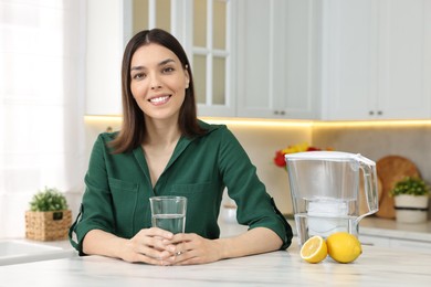 Photo of Woman with glass of water and filter jug in kitchen