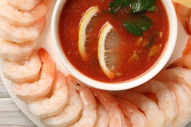 Tasty boiled shrimps with cocktail sauce and lemon on white wooden table, top view