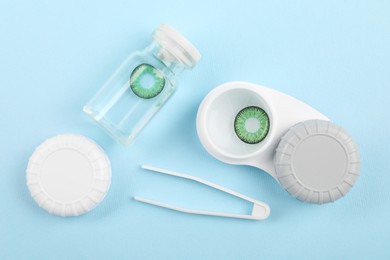 Photo of Bottle of solution, case with green contact lenses and tweezers on light blue background, flat lay