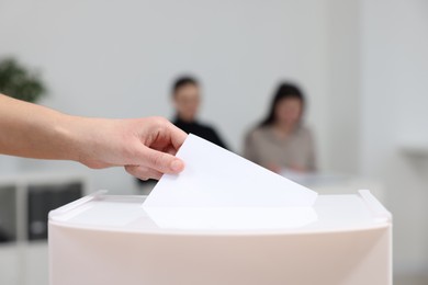 Photo of Woman putting her vote into ballot box on blurred background, closeup