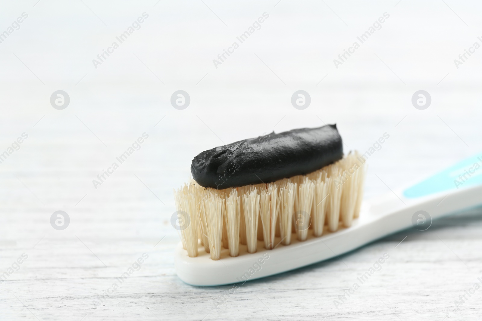 Photo of Toothbrush with natural bristles and charcoal paste on white wooden table, closeup