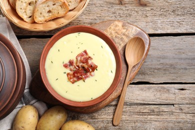 Photo of Tasty potato soup with bacon and rosemary in bowl served on wooden table, flat lay