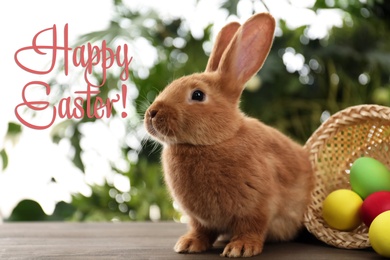 Image of Happy Easter! Cute bunny and basket with dyed eggs on table outdoors