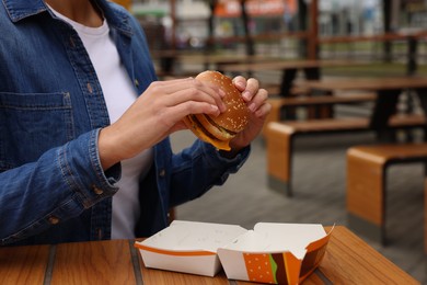 Photo of Lviv, Ukraine - October 9, 2023: Woman with McDonald's burger at wooden table outdoors, closeup