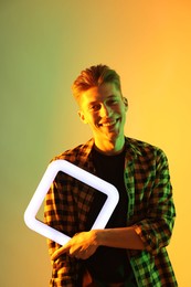 Photo of Young man with square lamp on color background in neon lights