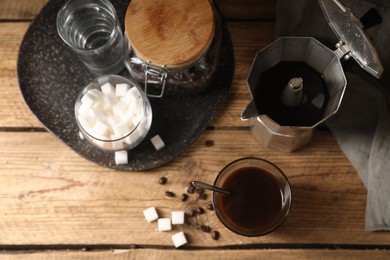 Photo of Brewed coffee in glass, sugar and moka pot on wooden table, flat lay