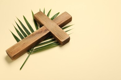 Photo of Wooden cross and palm leaf on beige background, space for text. Easter attributes