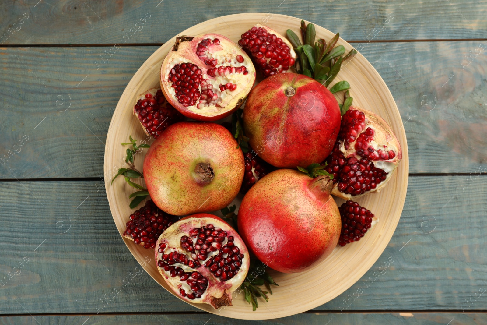 Photo of Delicious ripe pomegranates on blue wooden table, top view