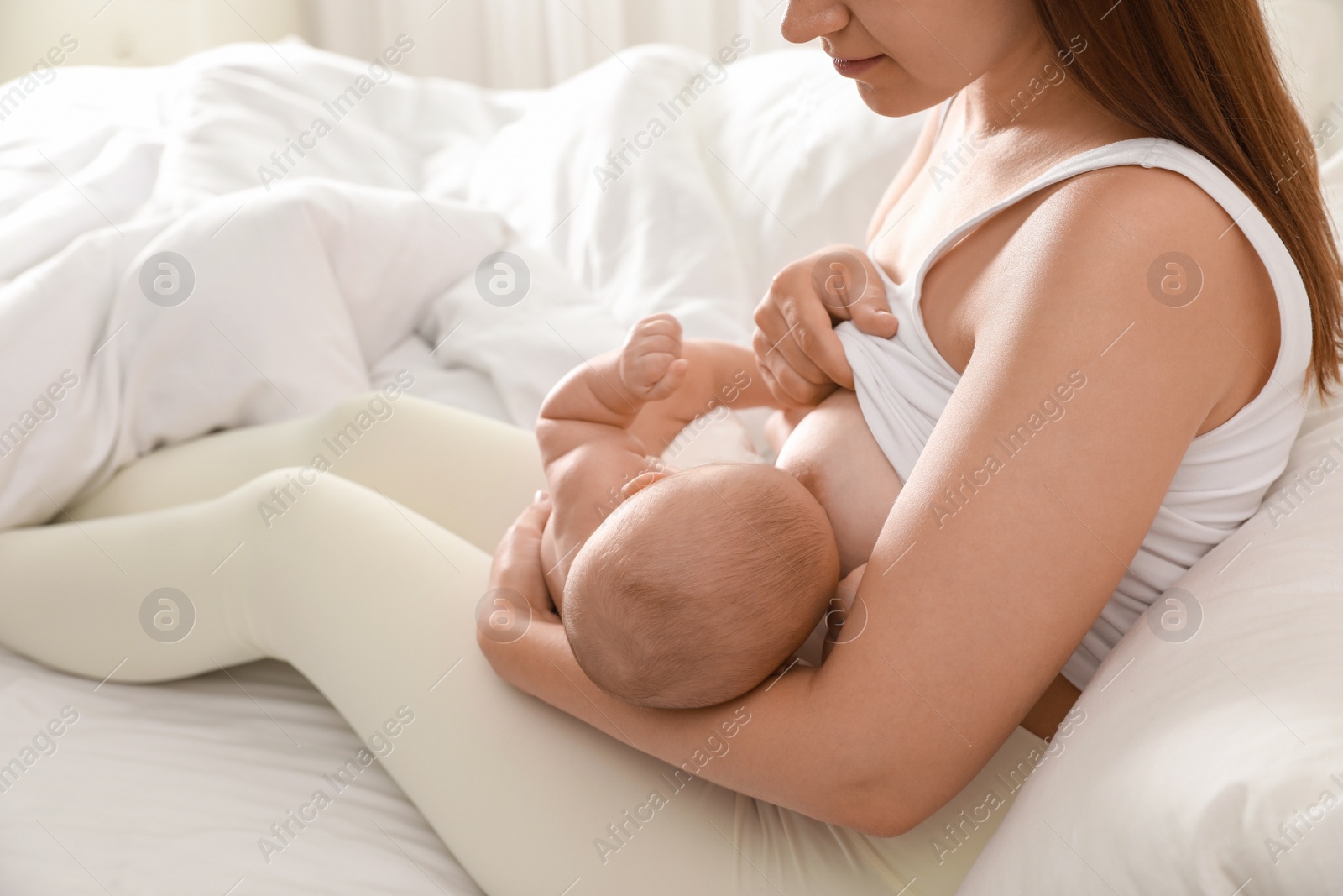 Photo of Young woman breastfeeding her little baby on bed at home, closeup