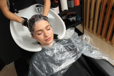 Hairdresser rinsing out dye from woman's hair in beauty salon, above view