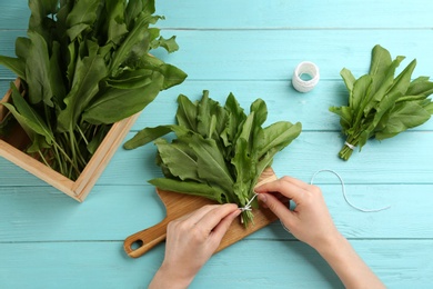 Photo of Woman tying bunch of sorrel leaves at light blue wooden table, top view
