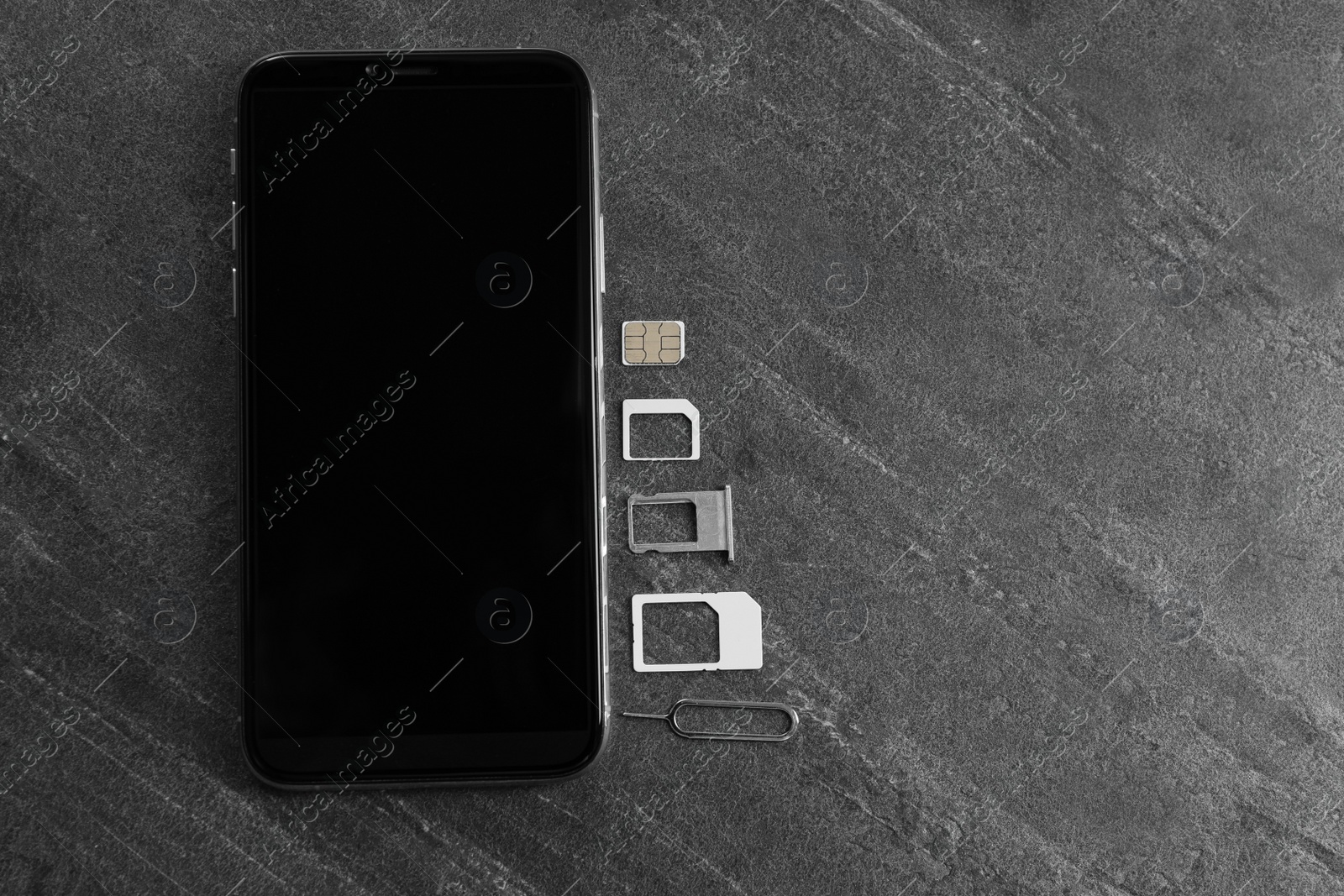 Photo of SIM card, mobile phone and ejector tool on grey table, flat lay. Space for text