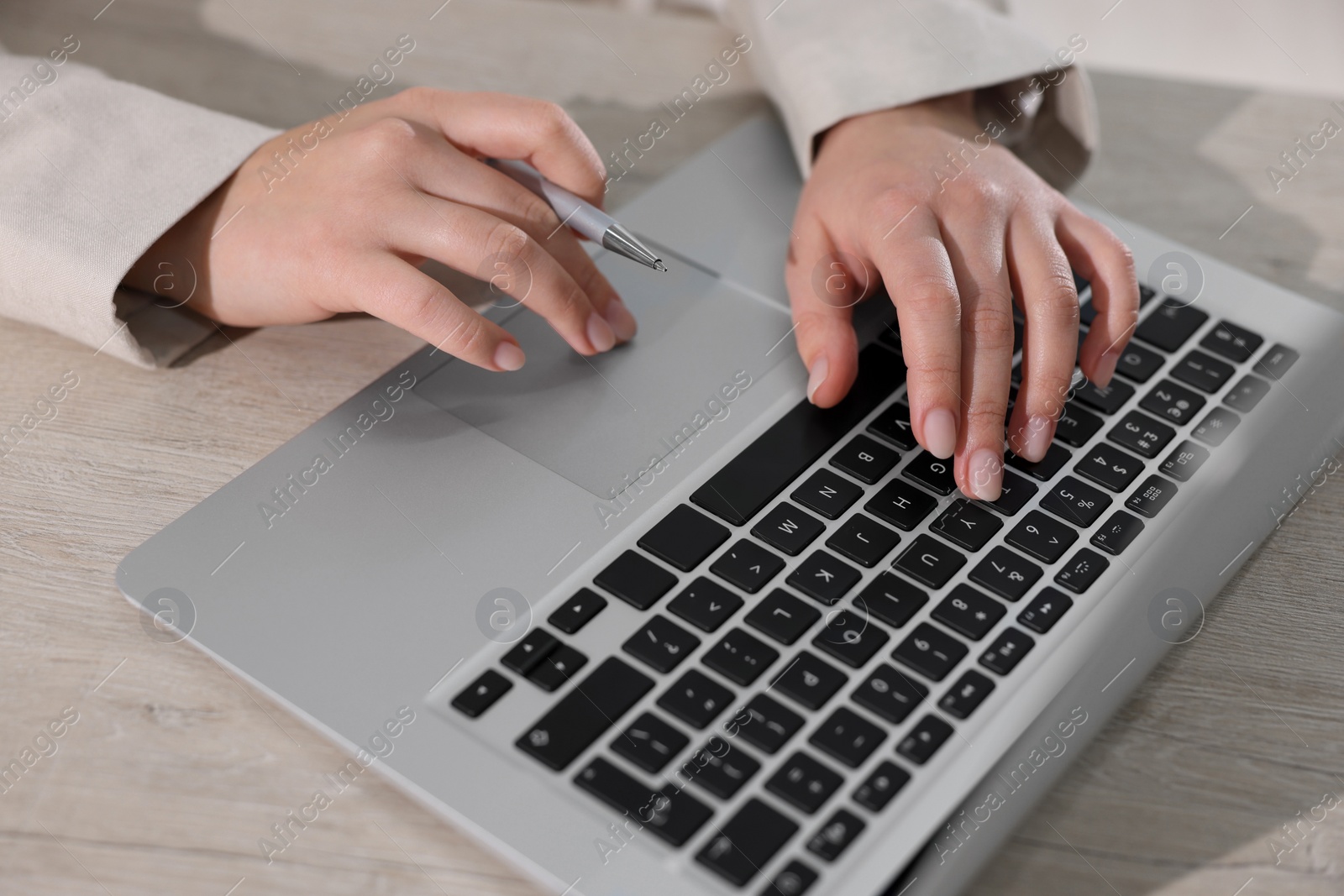 Photo of Woman with pen working on laptop at wooden table, closeup. Electronic document management