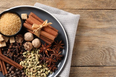 Photo of Plate with different aromatic spices on wooden table, top view. Space for text