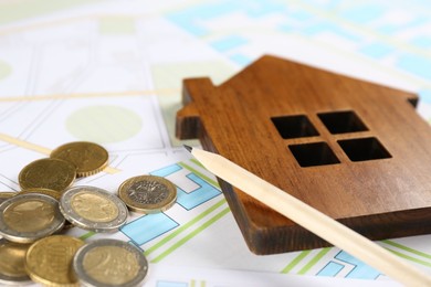 Photo of Coins, pencil and wooden house model on cadastral map, closeup