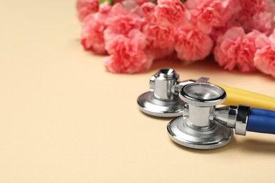 Happy Doctor's Day. Stethoscopes and beautiful flowers on beige background, closeup. Space for text