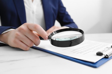 Photo of Woman looking at document through magnifier at white marble table, closeup. Searching concept