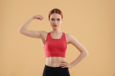 Photo of Young woman in sportswear showing muscles on beige background