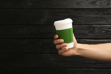 Woman holding takeaway paper coffee cup on wooden background. Space for text