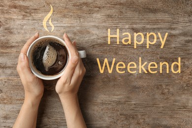 Happy Weekend. Young woman with cup of delicious hot coffee at wooden table, top view