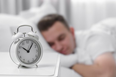 Man sleeping at home in morning, focus on alarm clock. Space for text