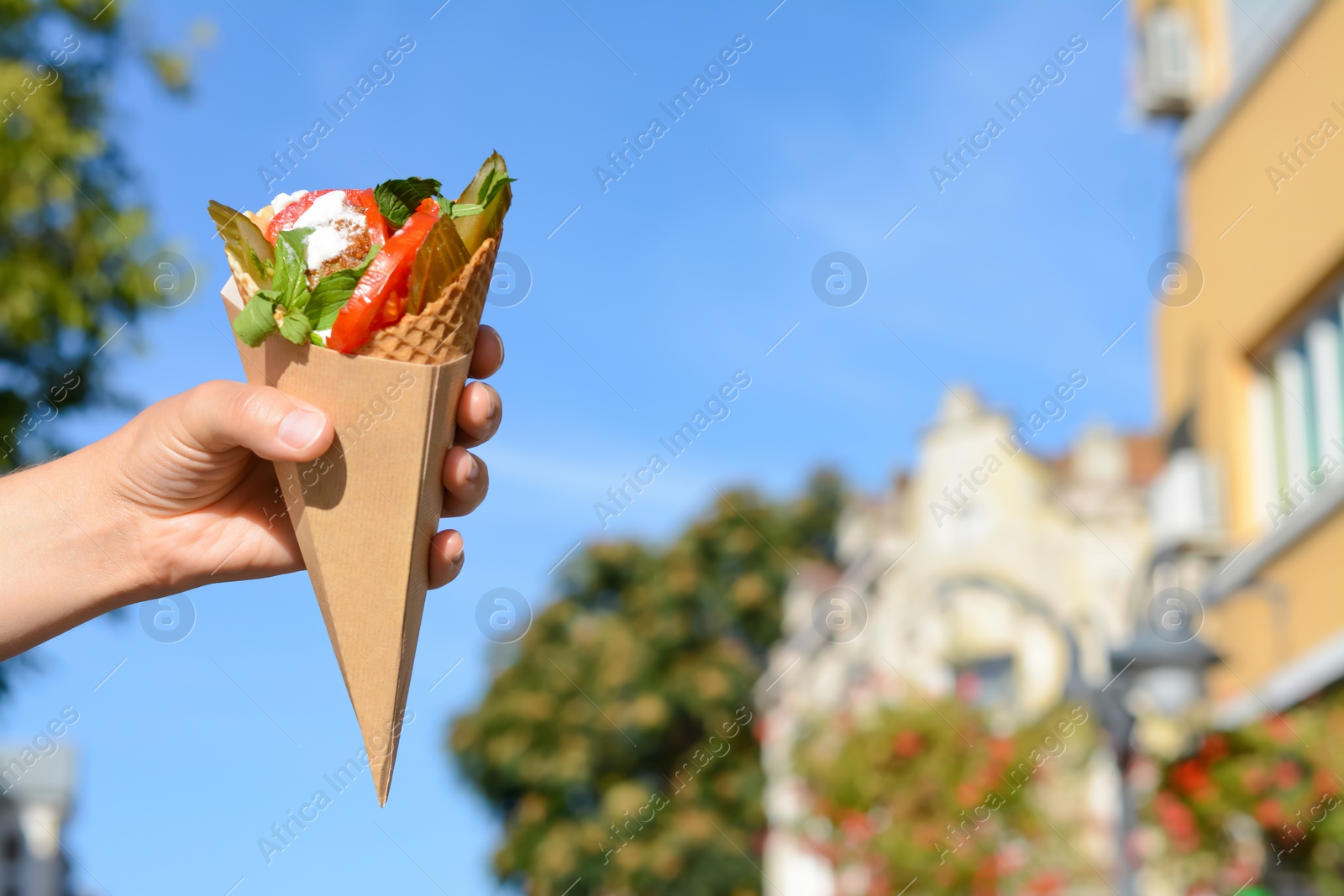 Photo of Woman holding wafer with falafel and vegetables outdoors, closeup. Space for text