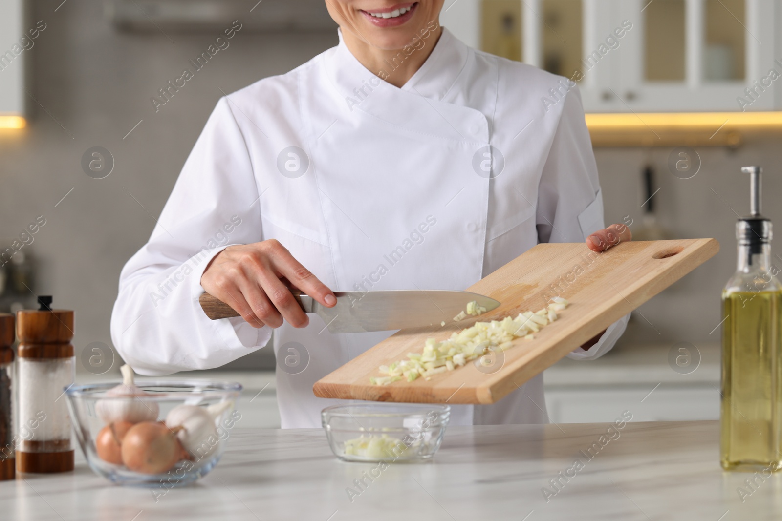Photo of Professional chef putting cut onion into bowl at white marble table indoors, closeup