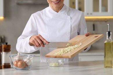 Professional chef putting cut onion into bowl at white marble table indoors, closeup