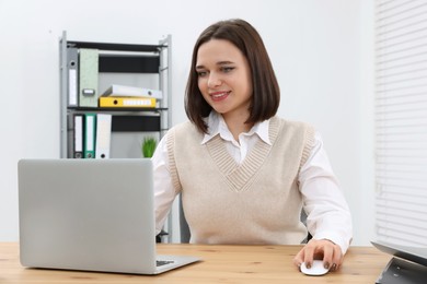 Photo of Happy young intern working with laptop at table in modern office