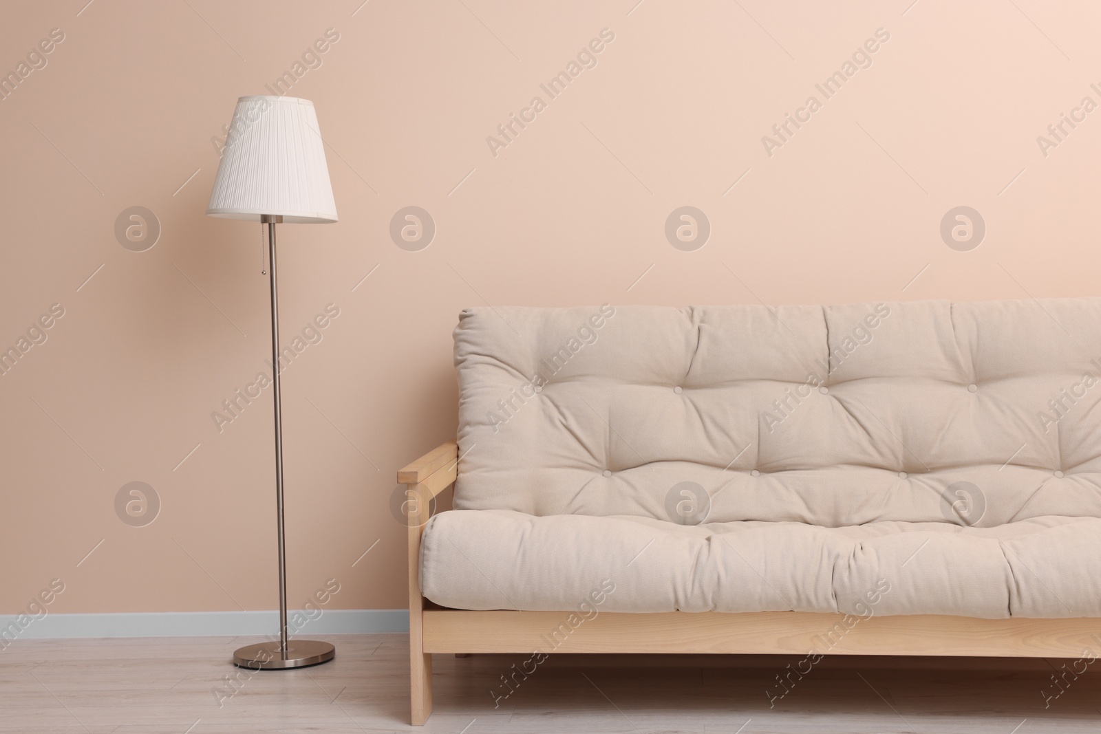 Photo of Comfortable sofa and stylish lamp near beige wall indoors