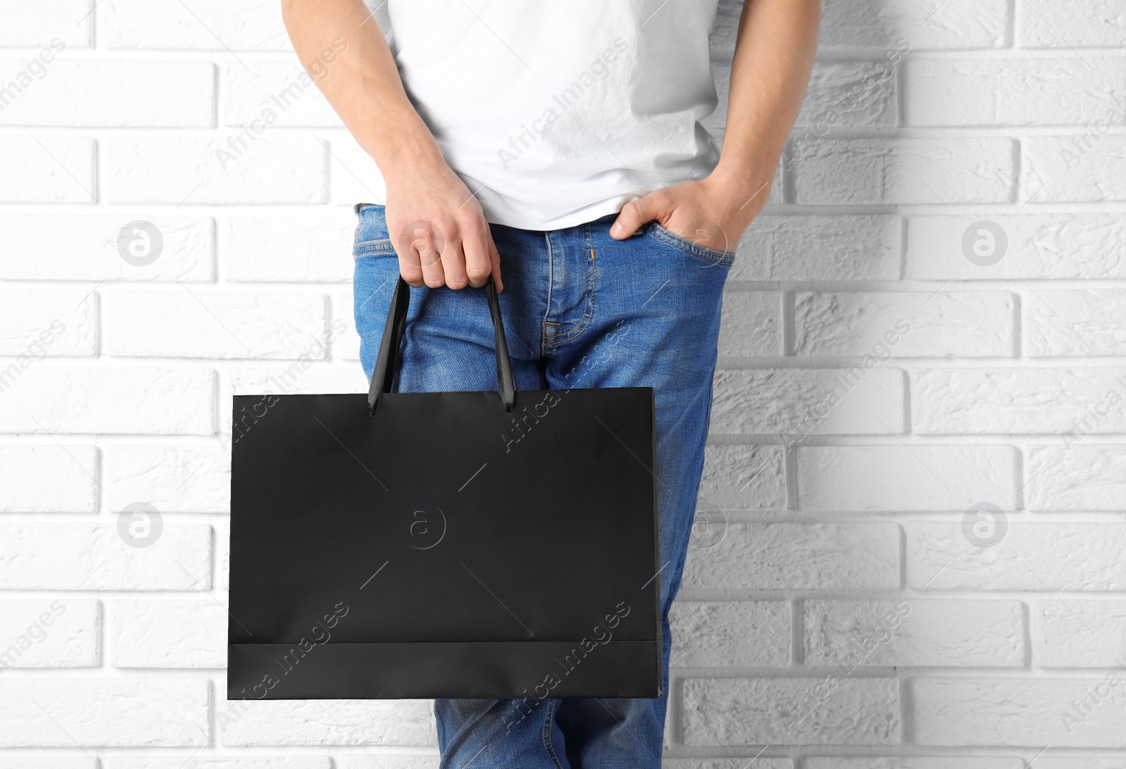 Photo of Man holding mock-up of paper shopping bag against wall