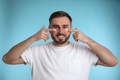 Happy young man applying facial cream on light blue background