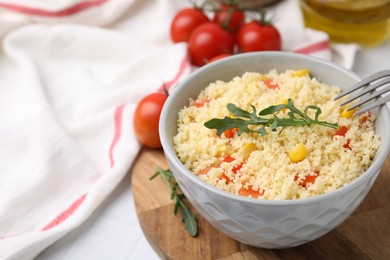 Bowl of tasty couscous with pepper, corn, arugula and fork on white table, closeup. Space for text