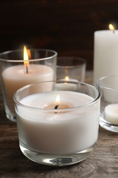 Burning wax candles in glasses on wooden table