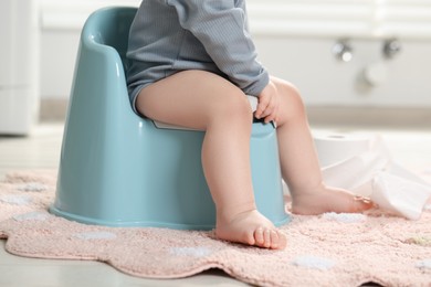 Photo of Little child sitting on plastic baby potty indoors, closeup