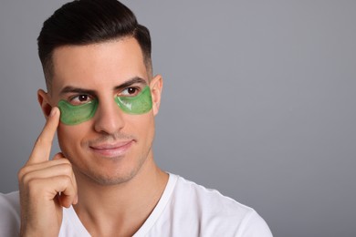 Photo of Man applying green under eye patch on grey background. Space for text