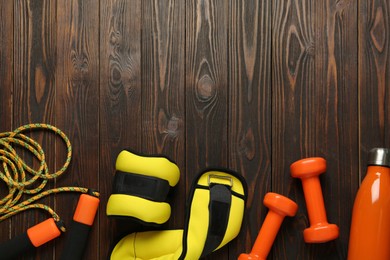 Photo of Yellow weighting agents and sport equipment on wooden table, flat lay. Space for text