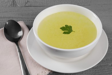 Photo of Tasty broth in bowl on grey wooden table, closeup