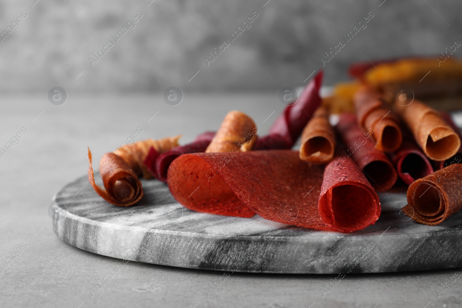 Photo of Delicious fruit leather rolls on grey table, closeup