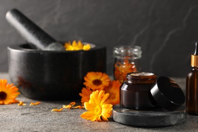 Jar of cream, mortar and beautiful calendula flowers on grey table, space for text